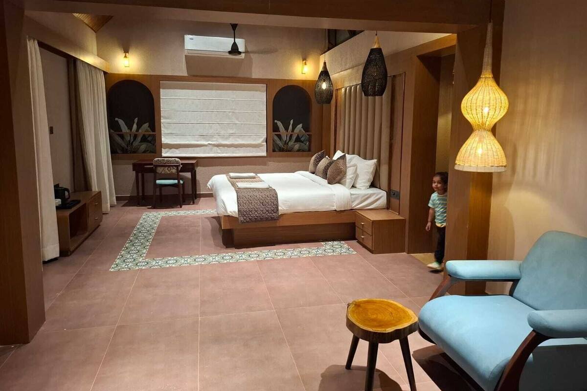 A bedroom with a bed, bedside tables, a desk, a chair, and a hanging light fixture.