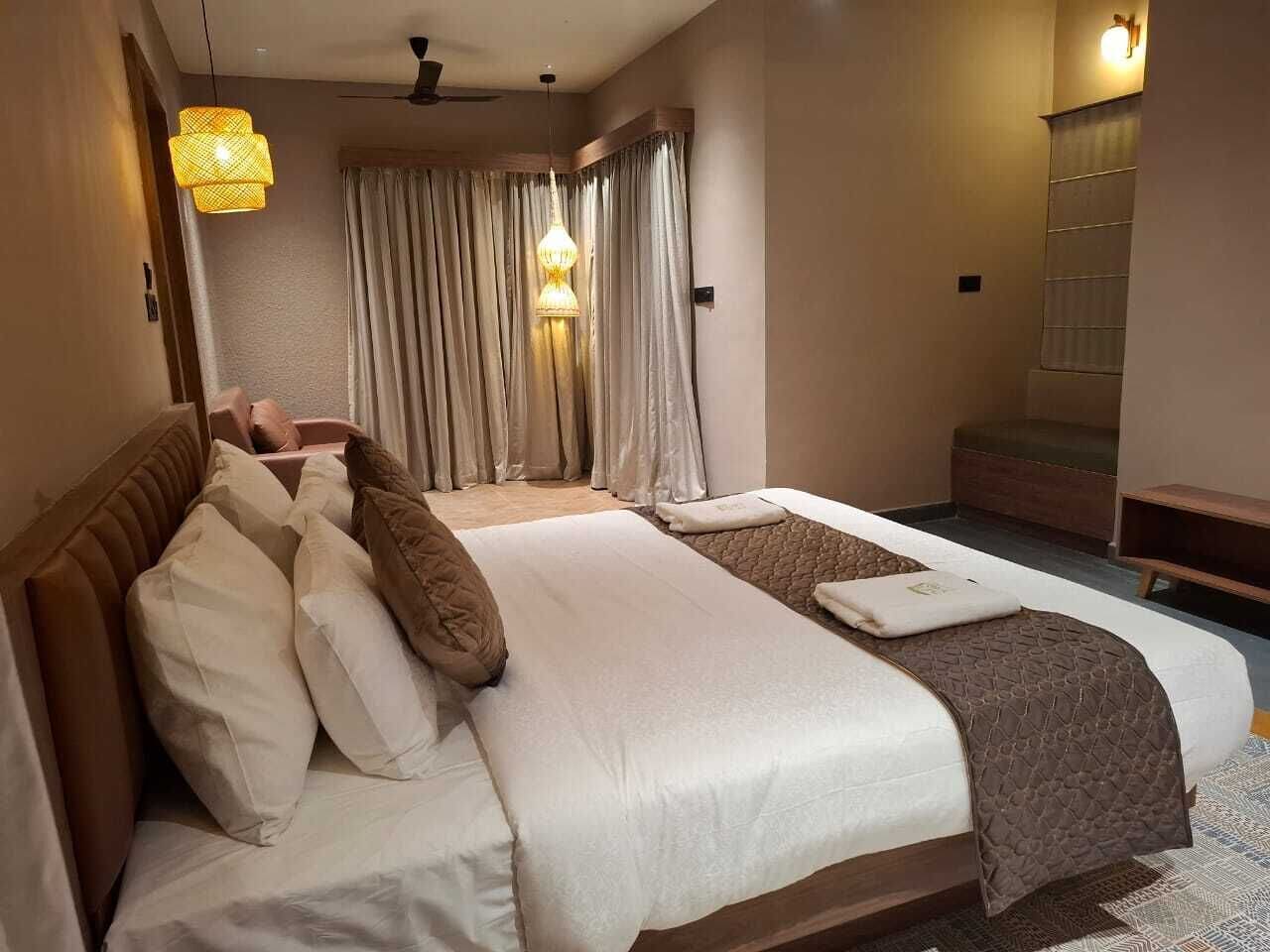 A hotel room with a large bed, a bedside table, a lamp, curtains, and a ceiling fan.