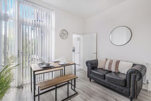 A modern living room with a dining table, a black leather sofa, a round mirror, and a clock on the wall.