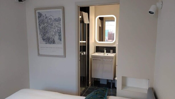 Una camera d'hotel con un letto, un'opera d'arte incorniciata, un bagno con uno specchio e una telecamera di sicurezza.