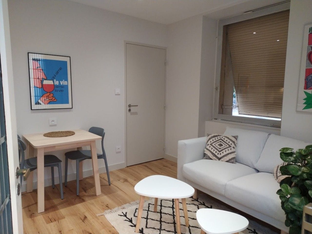 A living room with a white sofa, a small round table, and a dining table with chairs.