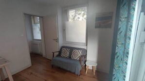 Una stanza con pavimento in legno, un divano con cuscini decorati, un tavolino rotondo e una finestra vista.