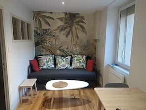 Ein Zimmer mit einer Couch, einem kleinen Tisch, einer Wandmalerei und einem Fenster.