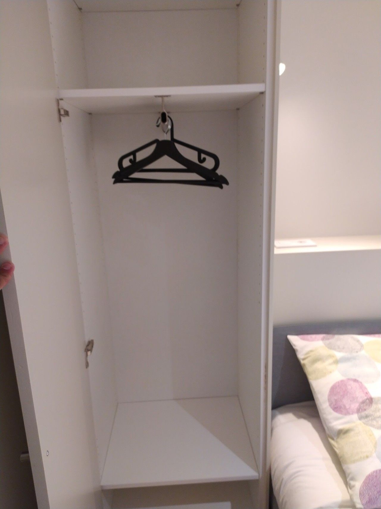 A bedroom with a bed, a hanging black hanger, and a white wardrobe.