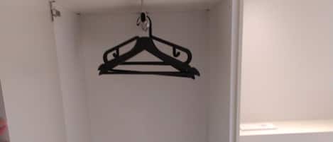 A bedroom with a bed, a hanging black hanger, and a white wardrobe.