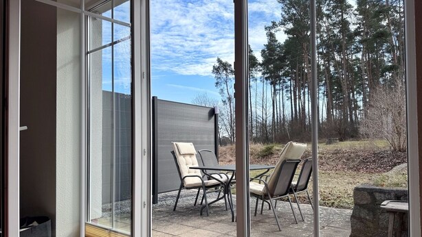 Quarto moderno com porta de vidro deslizante que dá para um pátio externo com duas cadeiras e uma mesa.