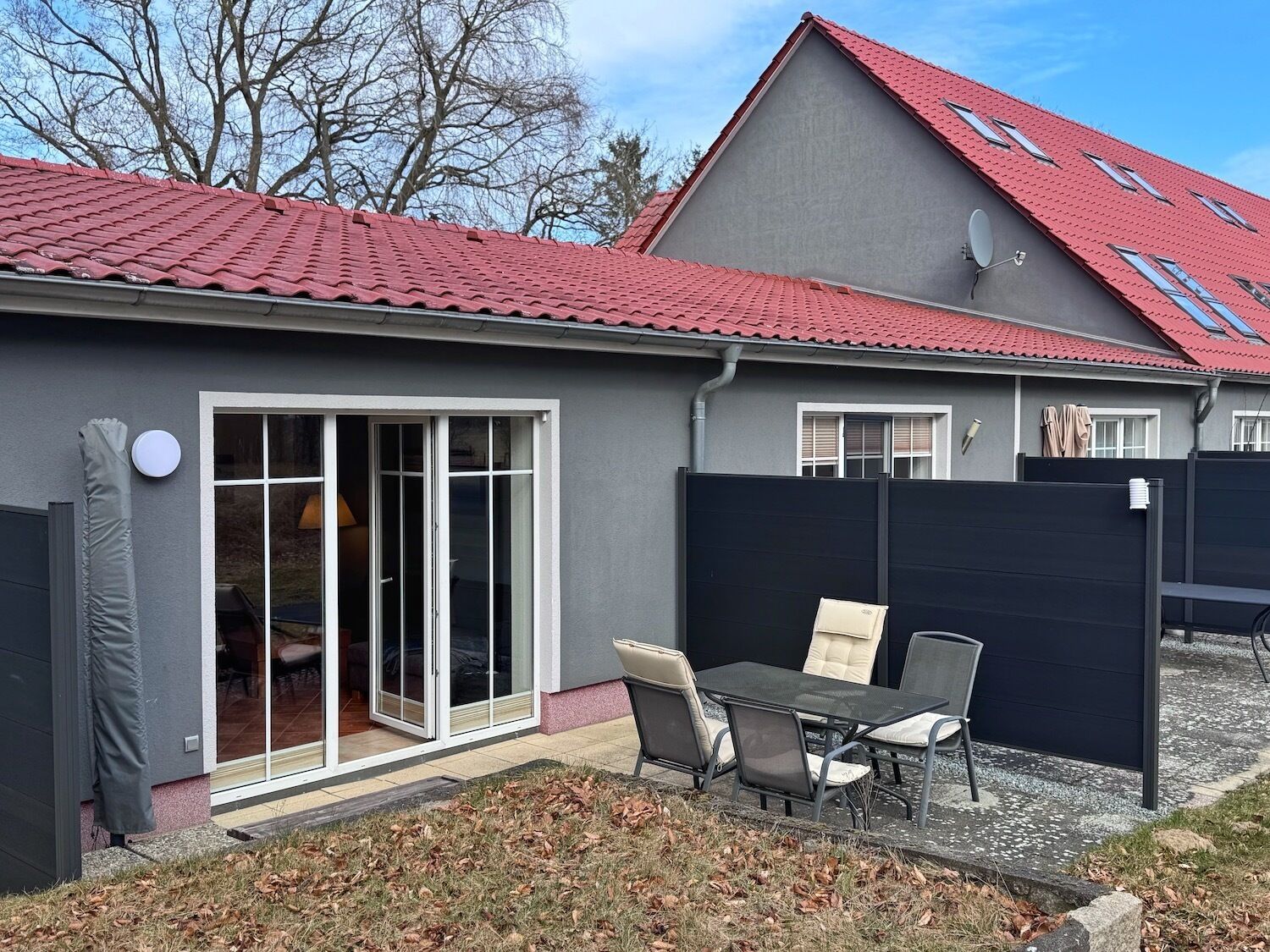 Una casa moderna con techo de tejas rojas, puerta corrediza de vidrio y patio con mobiliario exterior.