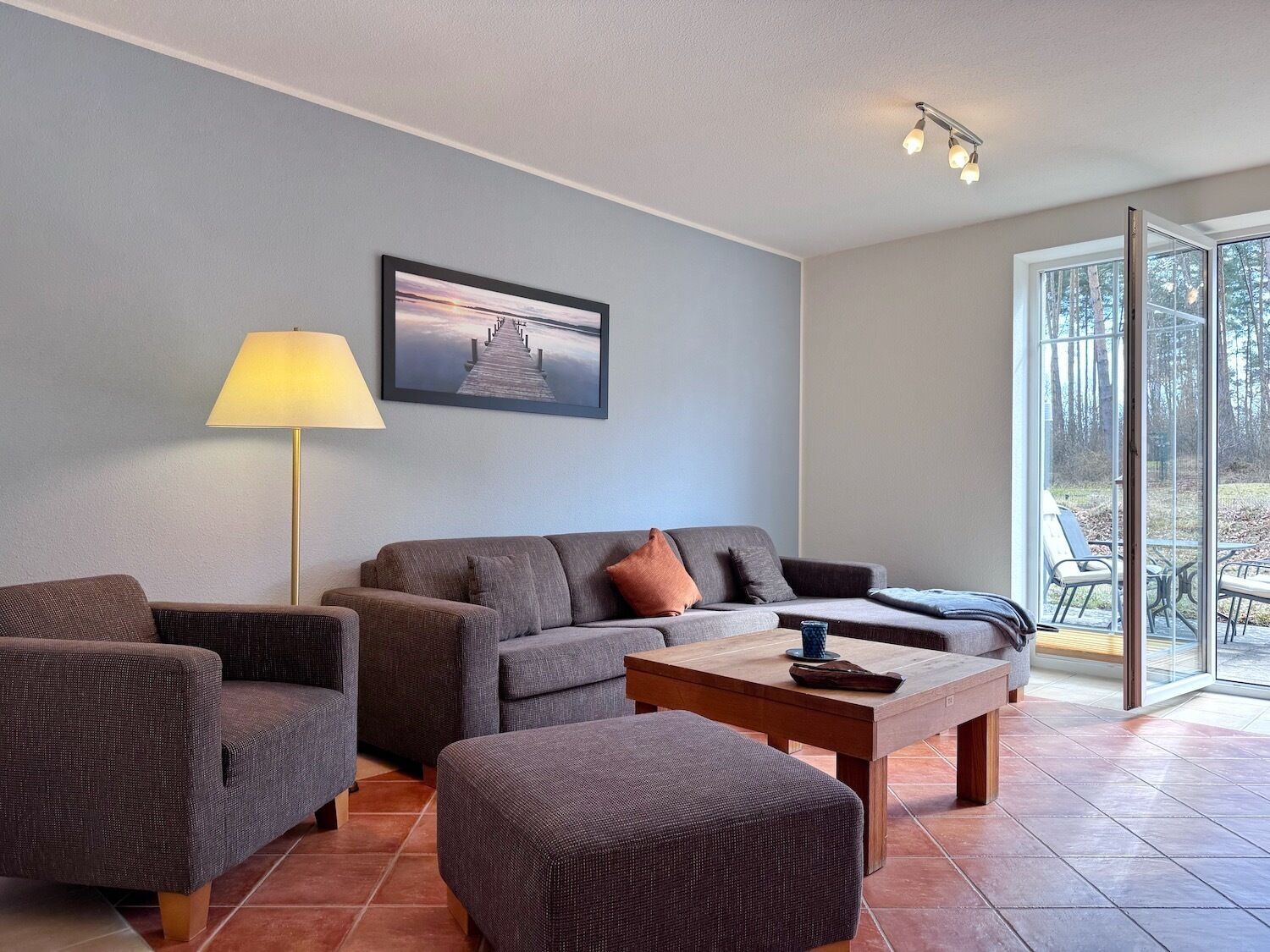 Un salón con sofá, dos sillones, una mesa de centro, lámpara y un cuadro en la pared.