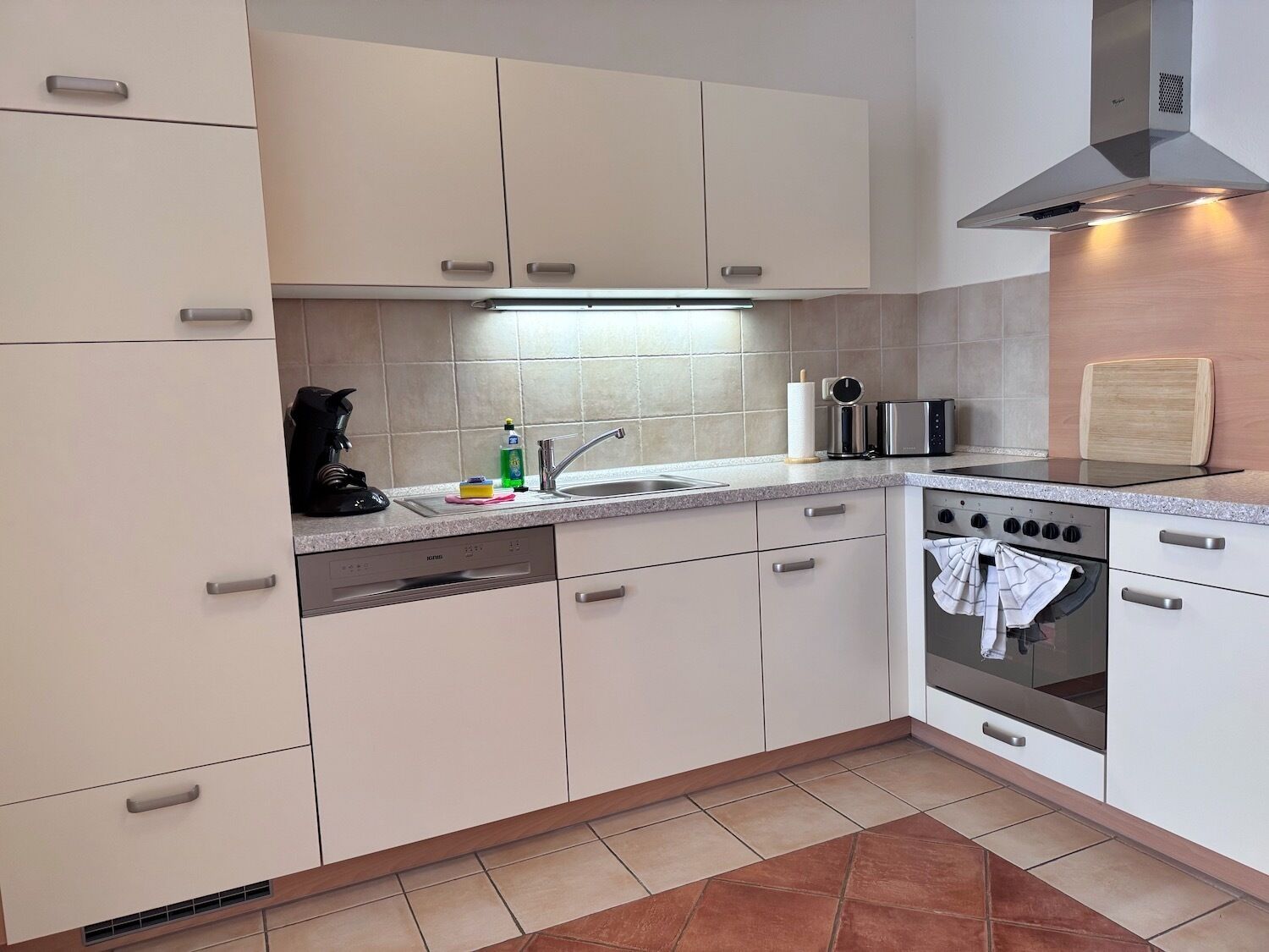 Una cucina moderna con mobili bianchi, una cappa aspirante in acciaio inossidabile, un forno integrato e una lavastoviglie.