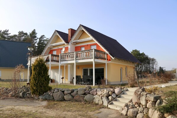 A two-story house with a balcony, a stone wall, and a clear sky. - Seeluft vacation home with lake view in Warin for a relaxing vacation (Warin)