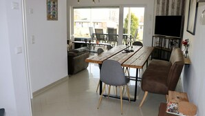 Ein Wohnzimmer mit einem Holzesstisch, grauen Stühlen, einem braunen Sofa und einem Fernseher auf einem Schrank.