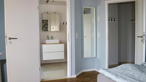 Ein Schlafzimmer mit Bett, Nachttisch, Kommode und einem Badezimmer mit Waschbecken und Spiegel.