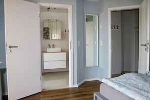 A bedroom with a bed, a nightstand, a dresser, and a bathroom with a sink and mirror. - Seeluft vacation home with lake view in Warin for a relaxing vacation (Warin)