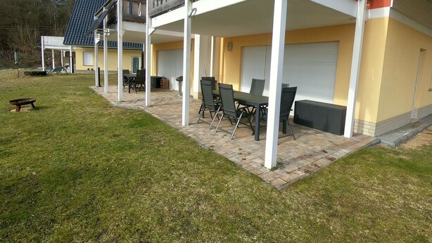 Ein zweistöckiges Gebäude mit überdachter Terrasse, Außenbereich mit Sitzgelegenheiten und Garage.