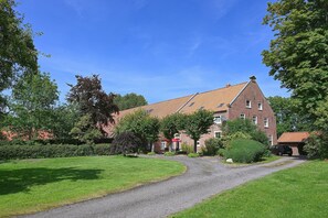A brick building with a sloped roof, surrounded by greenery and a gravel driveway. - Vacation apartment Fietje with wellness area in historic Gulfhof (Dornum)