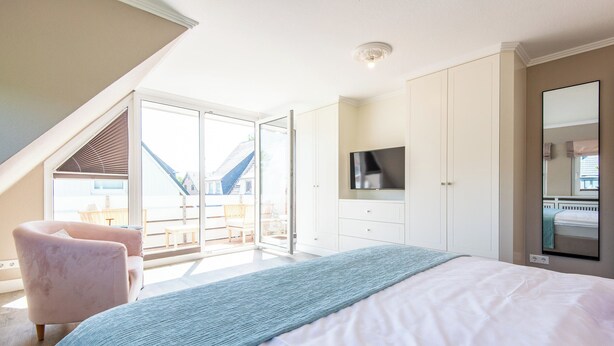 Ein Schlafzimmer mit Bett, Fernseher, großem Fenster und Balkon.