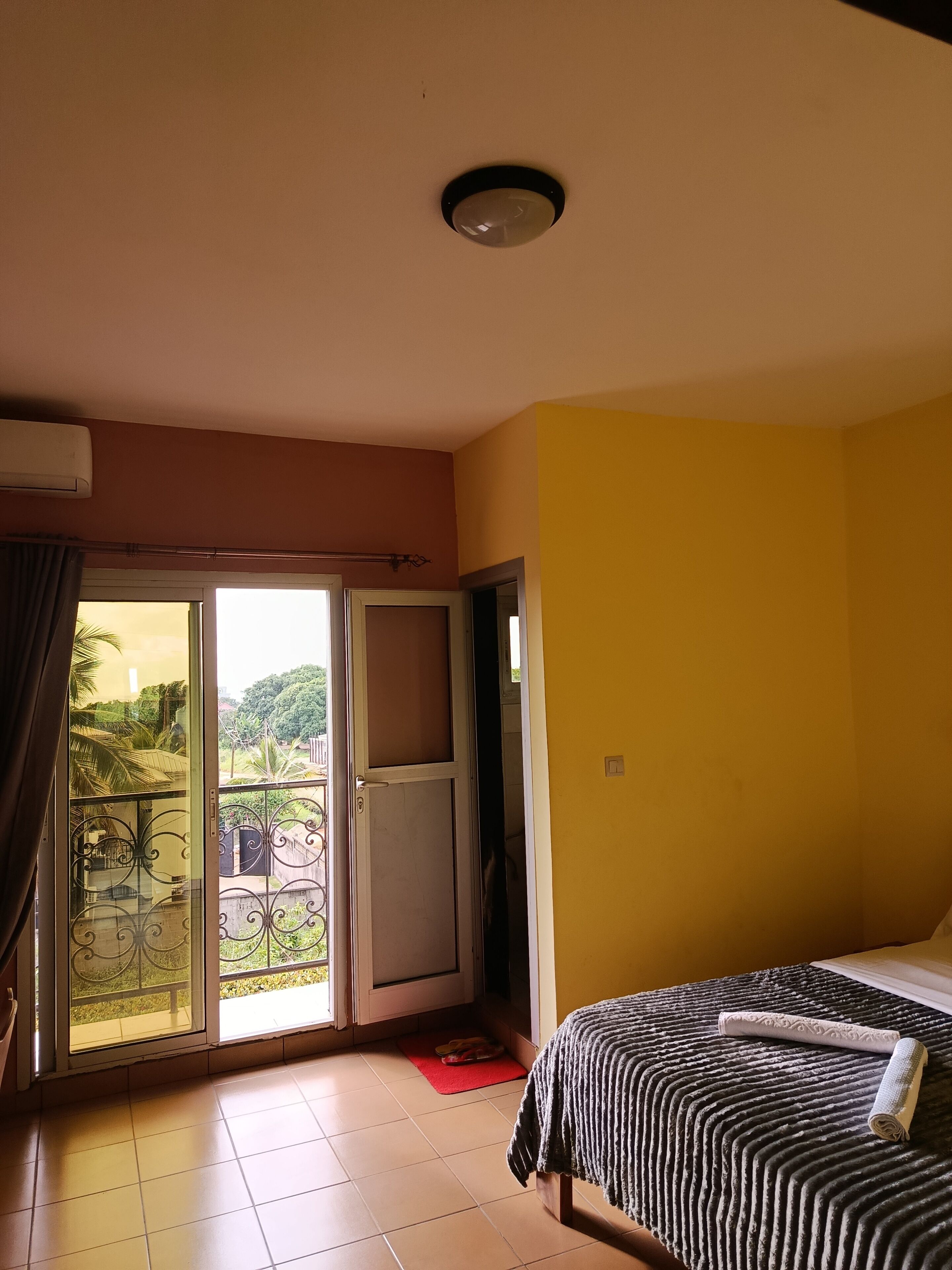 Una habitación con una cama, un tapete rojo, un balcón con vistas y una lámpara en el techo.