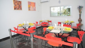 A dining area with red chairs and tables, white walls, and two paintings.