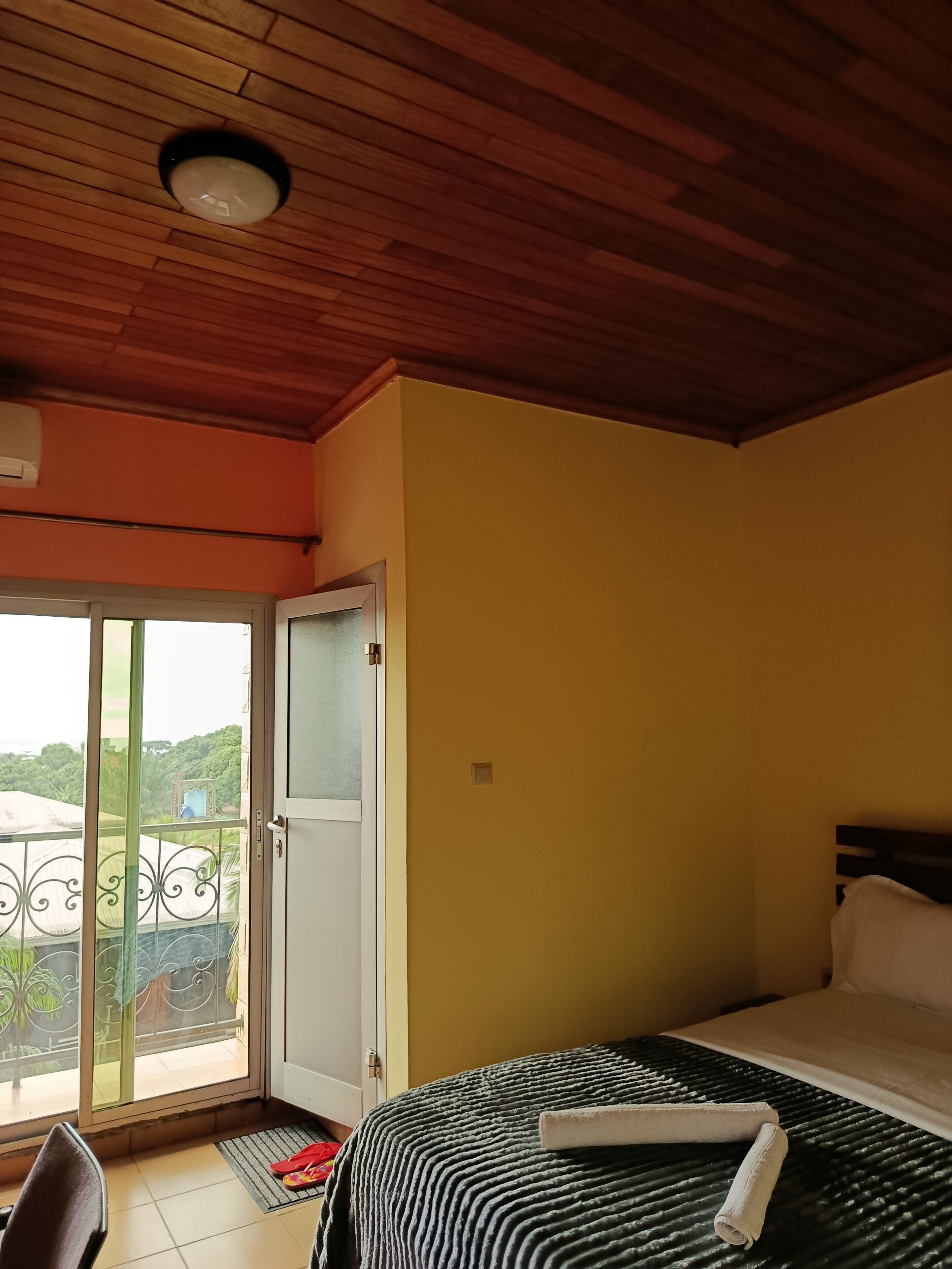 A room with a bed, a sliding glass door to a balcony, a ceiling fan, and a window.