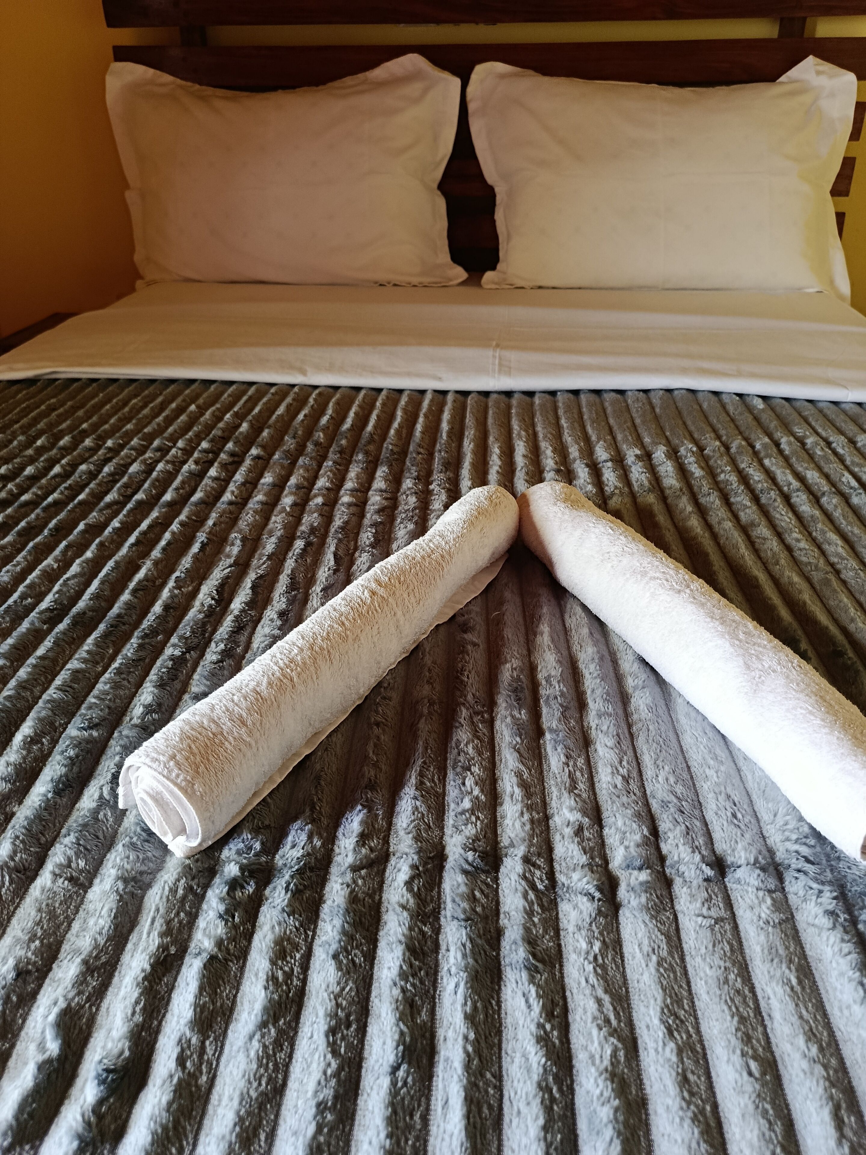 Una cama con una colcha a rayas, dos toallas enrolladas y almohadas blancas.