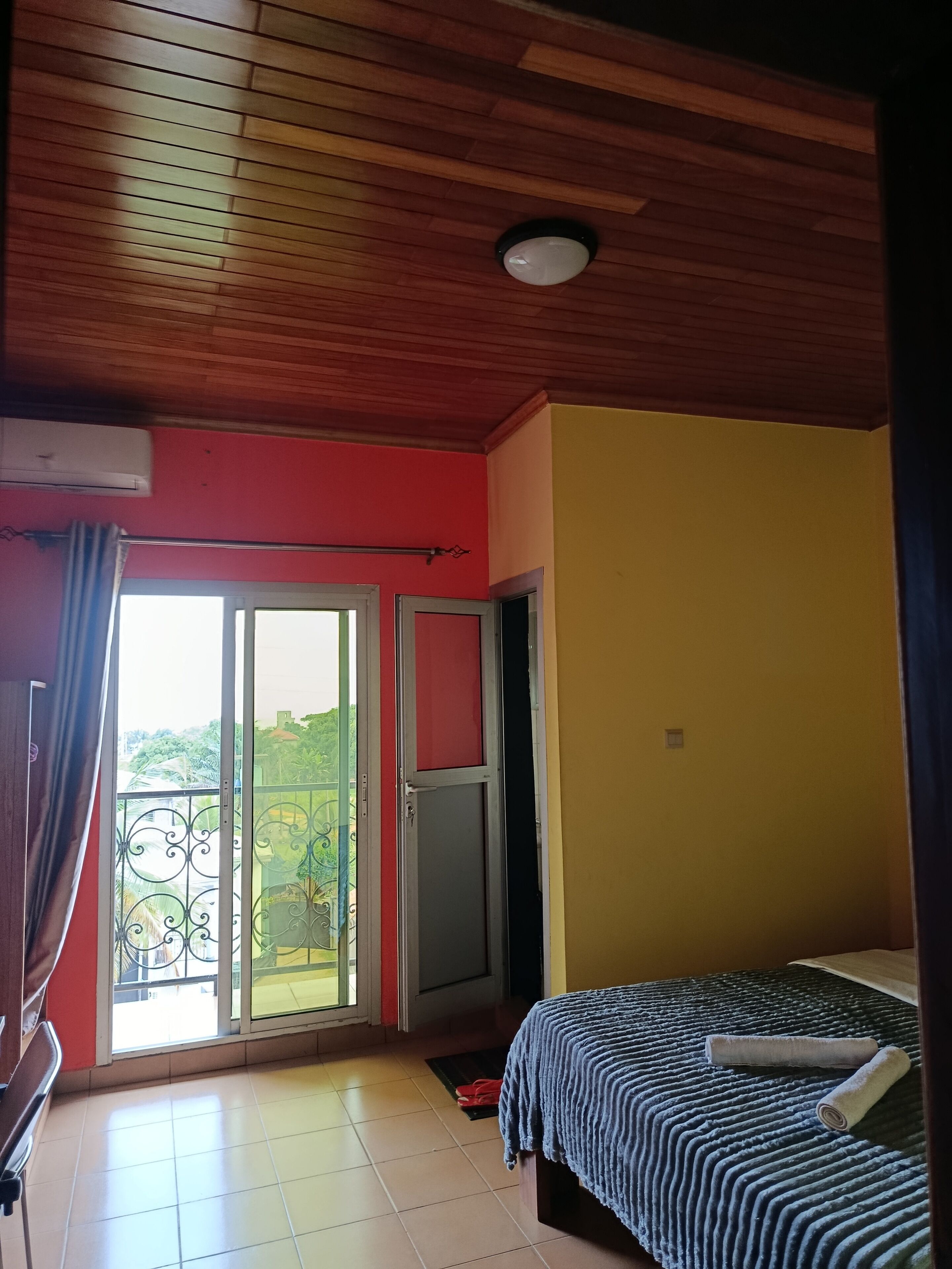 Una habitación con techo de madera, cama con manta a rayas, pared roja y puerta corrediza de vidrio que da a un balcón.