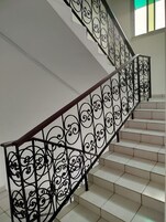 Una escalera con barandales de metal negro ornamentados y peldaños de baldosas blancas.