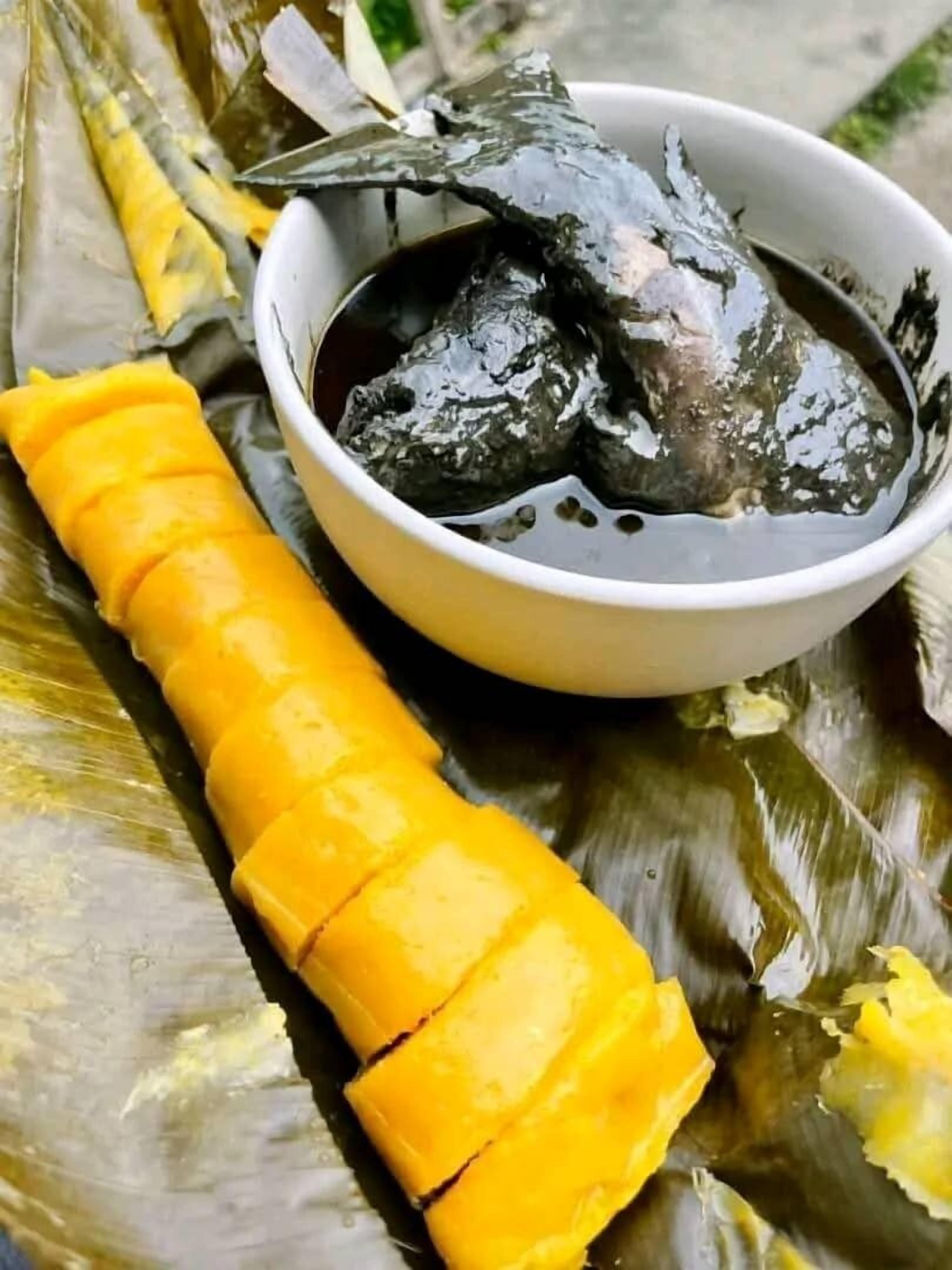 Un plat composé de tranches de mangue et d’un bol de sauce foncée, le tout servi sur une feuille de bananier.