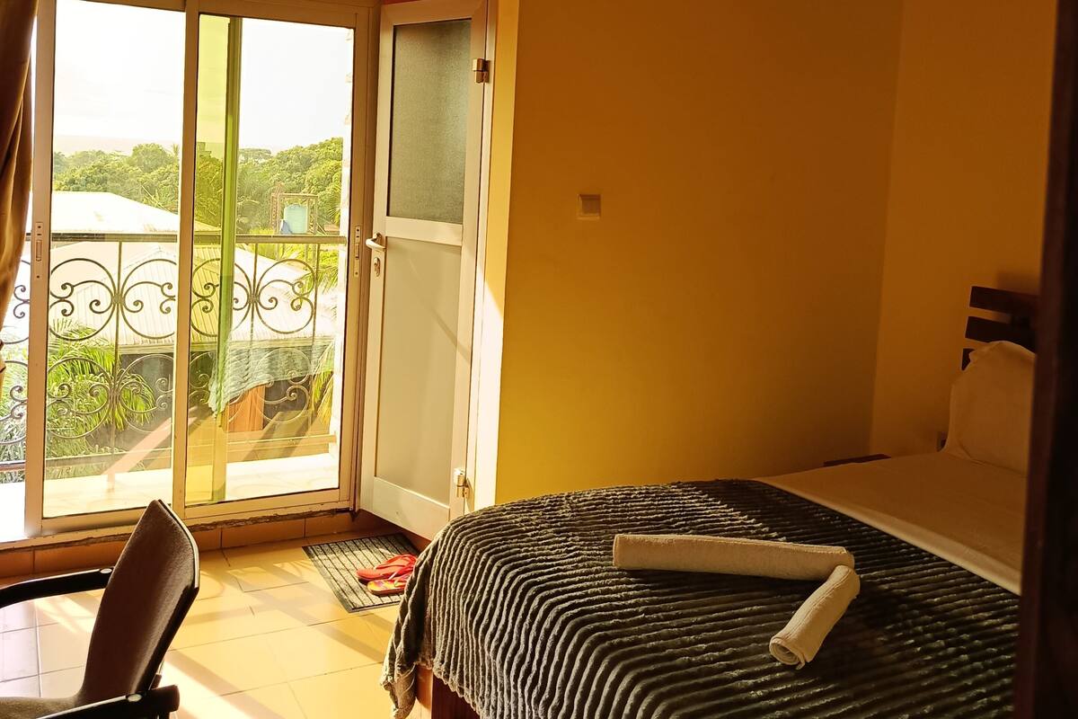 Una habitación con cama, una silla, un ventanal con vistas a la vegetación y una puerta.