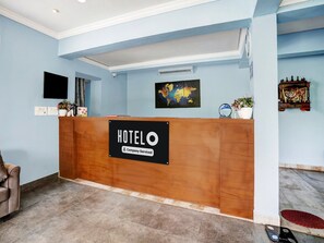 A hotel reception desk with a 'HOTELO Company-Serviced' sign, a flat-screen TV, a world map, and a small potted plant. - Deluxe Hotel Springs (Alto de Porvorim)