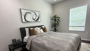 A bedroom with a bed, nightstands, a large window, a potted plant, and a wall art piece. - Backyard event space with basement apartment with kitchen, fitness room. (Fairburn)