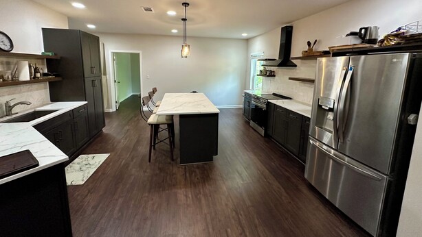 A modern kitchen with dark wood flooring, stainless steel appliances, and a central island. - Backyard event space with basement apartment with kitchen, fitness room. (Fairburn)