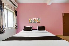 A hotel room with a bed, air conditioning unit, window with curtains, and three framed pictures on the wall.