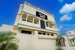 A hotel named 'HOTELO' with a modern architectural design, featuring a prominent sign, multiple balconies, and a gated entrance.