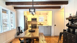 Una cocina con vigas de madera, una gran mesa de madera y un armario negro con tazas.
