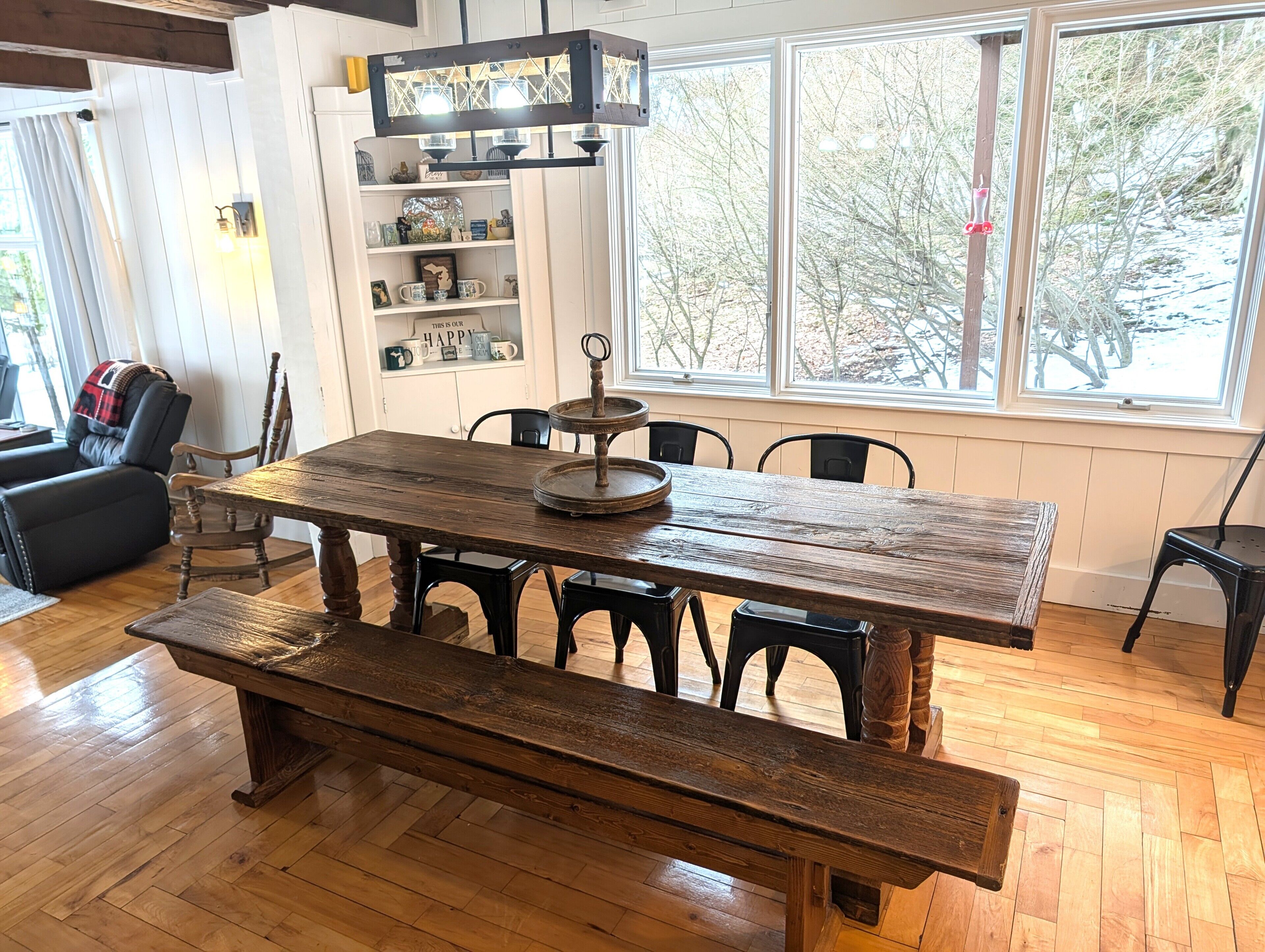 A dining area with a wooden table, benches, a chandelier, and a bookshelf.