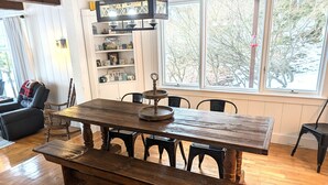 Un comedor con mesa de madera, bancos, una araña y una estantería.