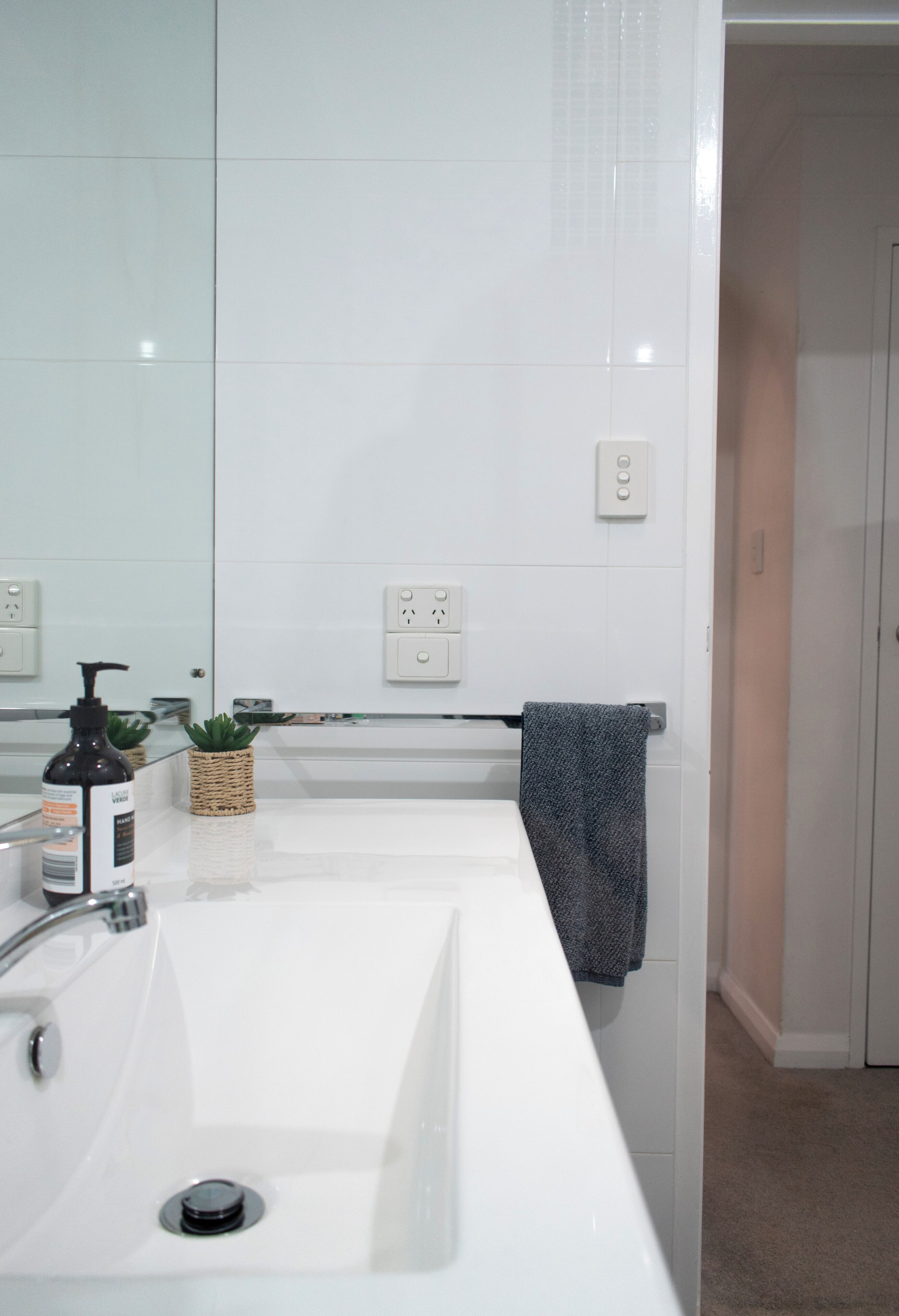 A bathroom with a white sink, a mirror, a towel rack, and a small plant.