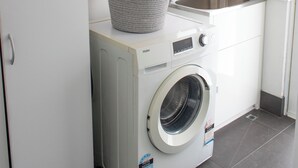 A compact laundry area with a washing machine, a sink, and a basket on the wall. - Family Friendly Coastal Oasis (Scarborough)