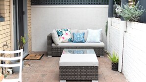 A wicker sofa with cushions, a small table, and potted plants in a patio area. - Family Friendly Coastal Oasis (Scarborough)