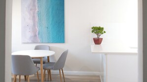 A dining area with a round table and four chairs, a painting of a beach, and a potted plant on a shelf. - Family Friendly Coastal Oasis (Scarborough)