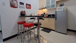 Eine kleine Küche mit Kühlschrank, Mikrowelle und Barhocker.