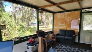 Ein gemütliches Zimmer mit einer Couch, Sesseln, einem kleinen Tisch und einem Fenster mit Blick auf Bäume.