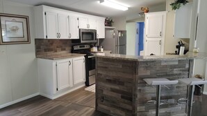 Eine moderne Küche mit weißen Schränken, einer Holztischinsel, Edelstahlgeräten und einer Bar mit Barhocker.