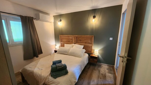 Ein Schlafzimmer mit Holz-Kopfteil, einem Bett mit weißer Bettwäsche, zwei Nachttischlampen und einem Fenster mit Vorhängen.