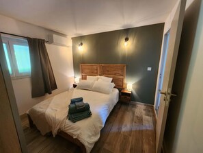 Ein Schlafzimmer mit Holz-Kopfteil, einem Bett mit weißer Bettwäsche, zwei Nachttischlampen und einem Fenster mit Vorhängen.