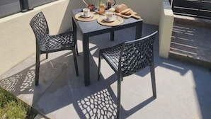 Eine Terrasse im Freien mit einem Tisch für zwei Personen, umgeben von Stühlen und einer kleinen Vase mit Blumen.