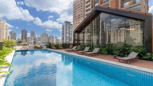 Piscina en la azotea con sillones de descanso y vistas a la ciudad.