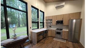 A modern kitchen with large windows, a dining area, and a view of a forest.