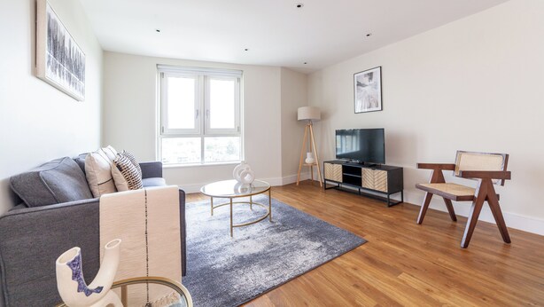 Una sala de estar moderna con un sofá, una mesa de centro, un mueble para la TV y una silla.