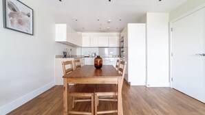 Un comedor con una mesa y sillas de madera, un jarrón y armarios blancos al fondo.